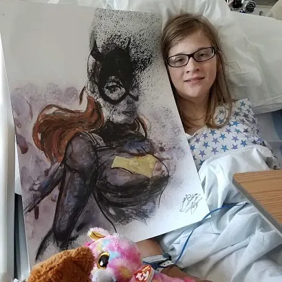 A patient in a hospital bed smiling with a Superman crest painting