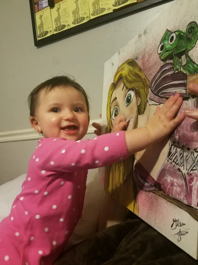 A little girl reaching up to touch a Rapunzel painting